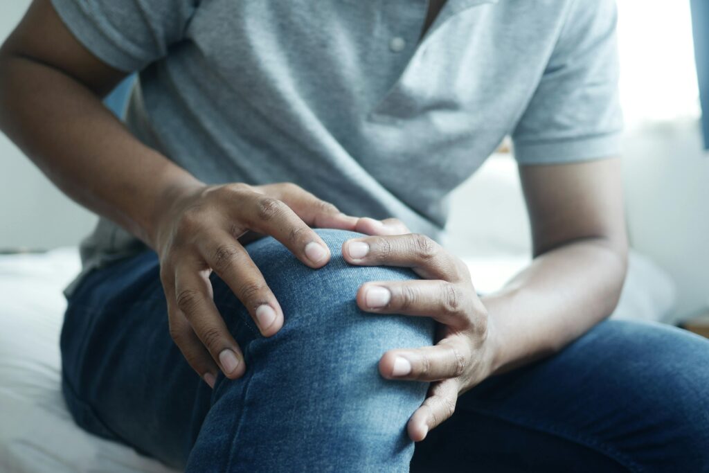 Manuelle Therapie gegen Gelenkbeschwerden im Knie Mann fasst sich an sein schmerzendes Knie